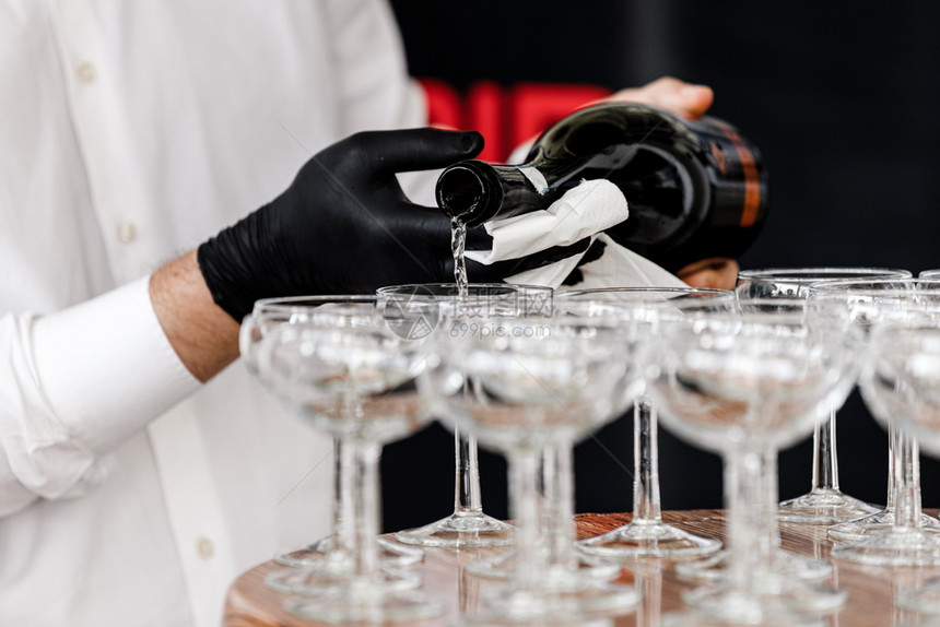 黑手套在餐厅里倒香槟黑手套服务员在木制桌子上倒香槟杯有选择的焦点黑手套在餐厅里倒香槟的手黑套服务员在木制桌子上倒香槟杯有选择的焦图片