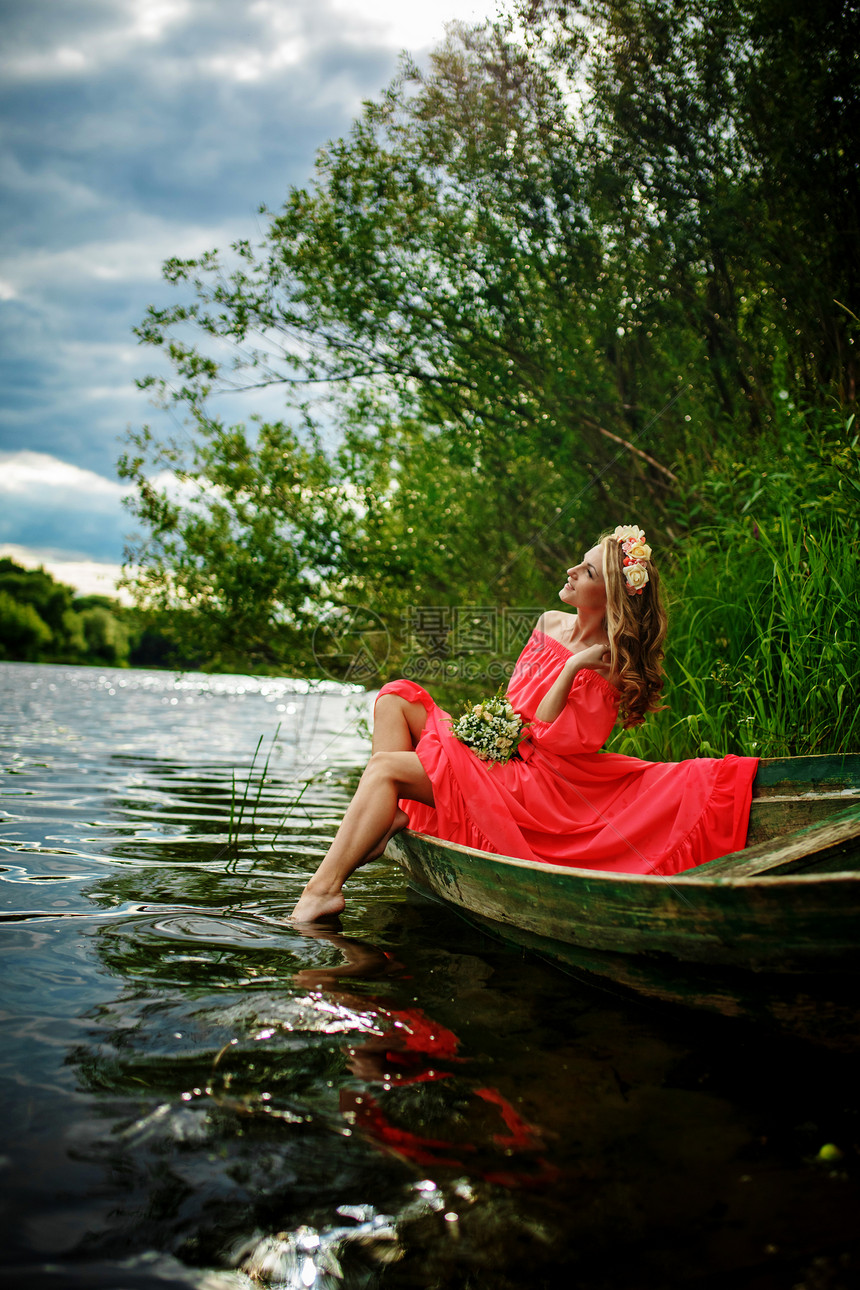 年轻感女人在船上穿红色衣服女孩头上戴花圈在河放松和沉睡图片
