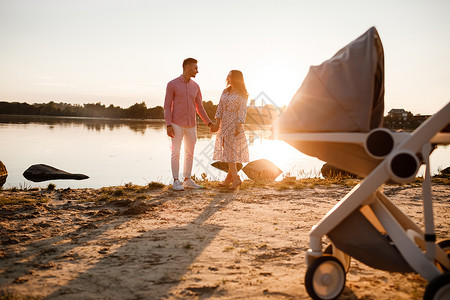 年轻的夫妇带着婴儿推车在湖边散步图片