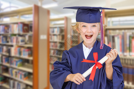 可爱的白人男孩穿着毕业帽子和礼服在图书馆文凭高清图片素材
