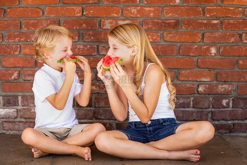 可爱的卡西亚小男孩和女吃西瓜与砖墙图片