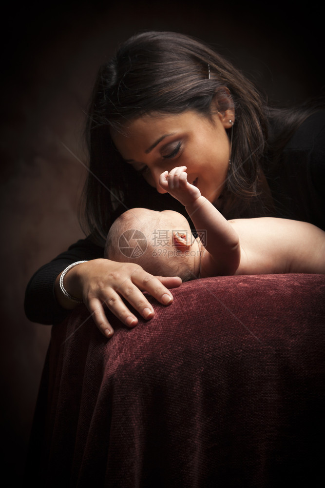 年轻有吸引力的少数民族妇女将新生婴儿放在引人注目的照明下图片