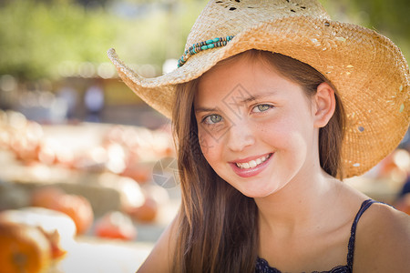 年轻前女孩的肖像穿着牛仔帽在南瓜草地生锈的设置高清图片
