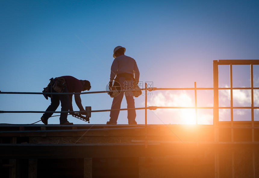 夕阳下建筑工人在屋顶上的背景图片