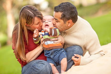 父母和婴儿开心的在公园玩耍亲吻着婴儿图片