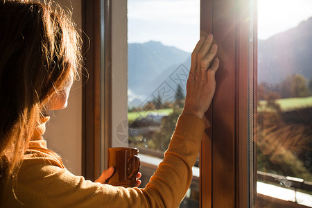 女孩拿着一杯咖啡看窗外的山上背景图片