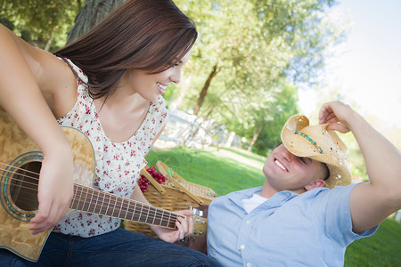 快乐的有吸引力混合种族夫妇吉他和牛仔帽在公园背景图片