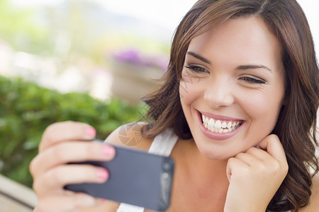 年轻笑的成女在长椅上户外的手机发短信欧洲的高清图片素材