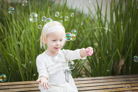 可爱的小女孩坐在长椅上和外面的泡玩得开心图片