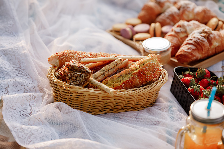 法国的羊角面包和新鲜果子在草地上供养两个人面布满粉红色的花瓣有选择焦点野餐在大自然新鲜的糕点羊角面包法国的羊角面包和新鲜果子图片
