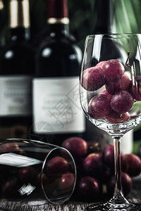 装满红葡萄的酒杯各种红葡萄酒瓶子木碗里的坚果和背景新鲜葡萄背景图片