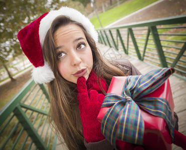 穿着圣诞帽子佩戴包装礼物并在外面鞠躬的漂亮喜悦微笑的女人图片