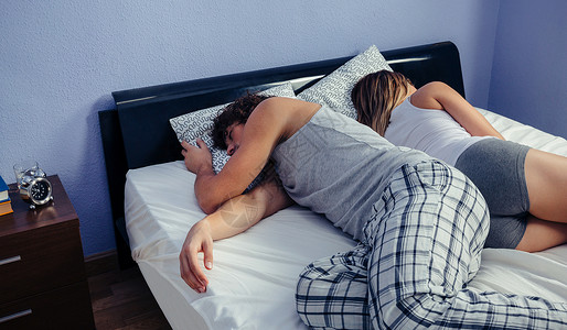 年轻夫妇睡在被揭开的床上背背景图片