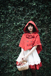女孩穿着斗篷在绿树公园穿着小红色兜帽装饰的年轻女子肖像背景