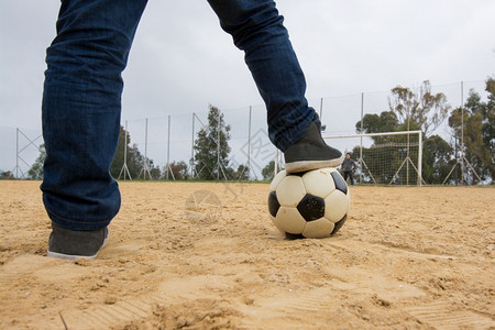 小男孩的脚躺在足球的顶上沙旧田地上图片