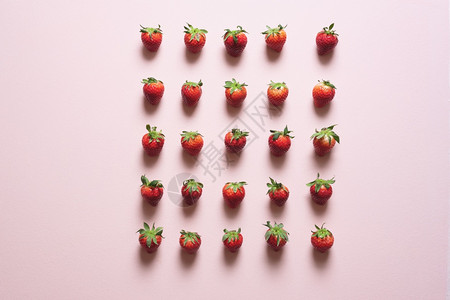 有机草莓水果排列在行内各间距离相等粉红色桌子上的新鲜草莓在上视图中图片