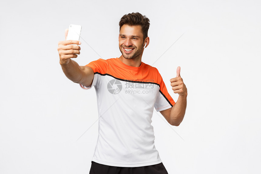 英俊的男运动员穿着无线耳机运动服自拍在智能手机上自拍展示拇指和微笑的快乐建议健身提倡康的生活方式和锻炼英俊的男运动员穿有无线耳机图片
