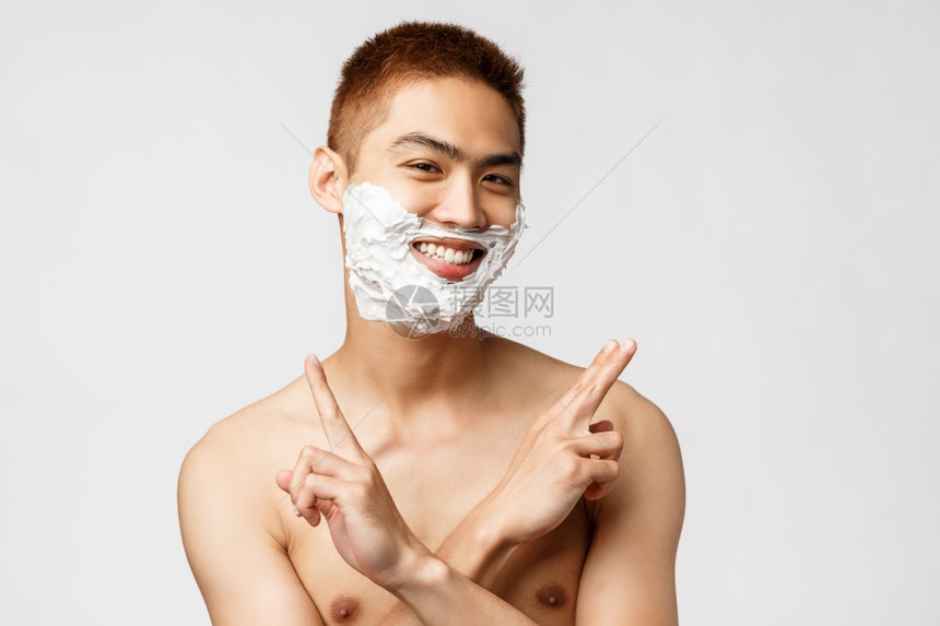 美貌人与卫生概念有趣的少龄青年男子第一次刮胡在上涂奶油微笑用交叉手展示和平迹象赤身站立美丽用赤身站立图片