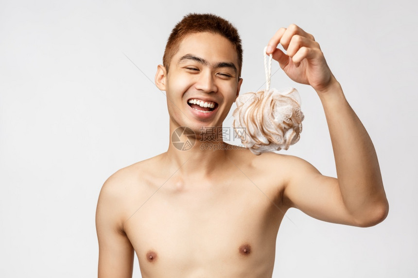 美丽人与卫生概念快乐的年轻英俊亚洲男子赤身地站在白背景上拿着淋浴海绵和笑在运动锻炼后洗澡美貌快乐的年轻英俊亚洲男子站在白背景上握图片