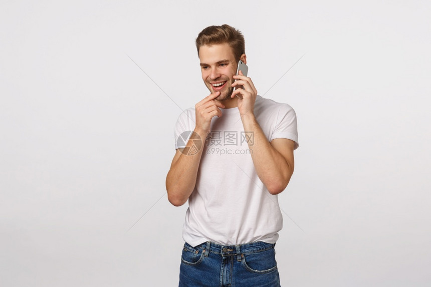 有趣的快乐金发男子通过电话接受邀请晚会将智能手机贴近耳朵用手机聊天触摸嘴唇微笑诱人交谈白背景图片