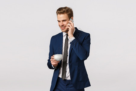 耳朵经济迷人自信和优雅的年轻长胡子男穿着经典西装手持智能机近耳从办公室打给妻子喝杯咖啡工作公司交易和商业概念穿着经典西装喝杯咖啡背景