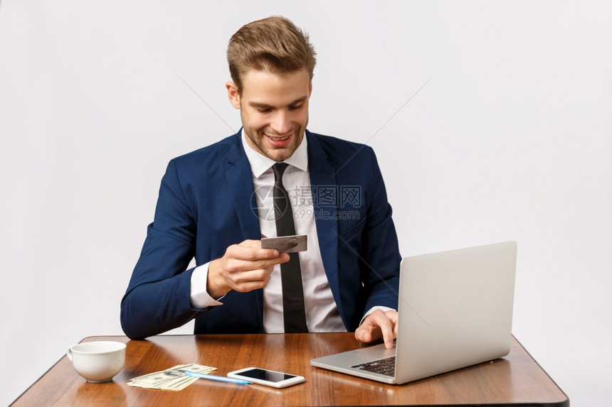英俊的年轻商人在办公张贴线订单通过笔记本电脑插入银行细节购物网站持有信用卡等待作为智能手机用钱撒谎表的电话英俊年轻商人在办公设置图片
