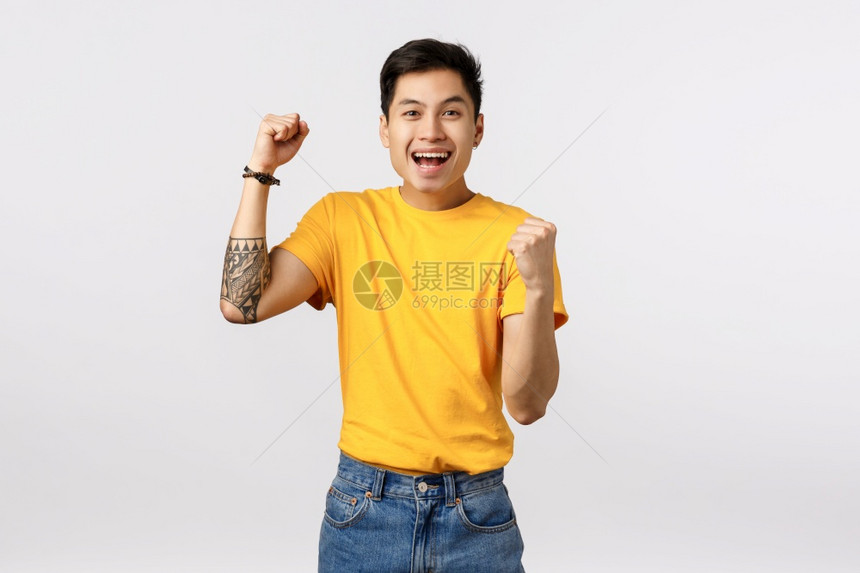 欢乐的年轻纹身男子穿着黄t恤拳头泵鼓励支持球员出价微笑快乐成为冠军庆祝胜利欢呼为您做得很好欢乐的年轻纹身男子穿黄色t恤为球员扎根图片
