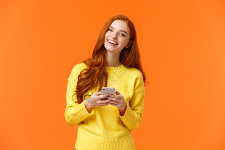 使用智能手机笑持有手机聊天或浏览社交网络橙色背景图片
