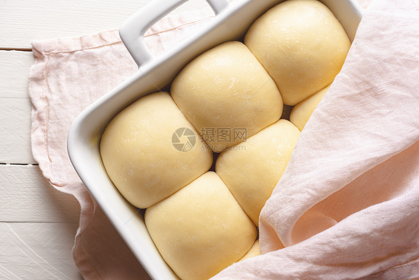 用粉色毛巾覆盖的瓷盘中未烤面包准备烘烤的酸面包上的团图片
