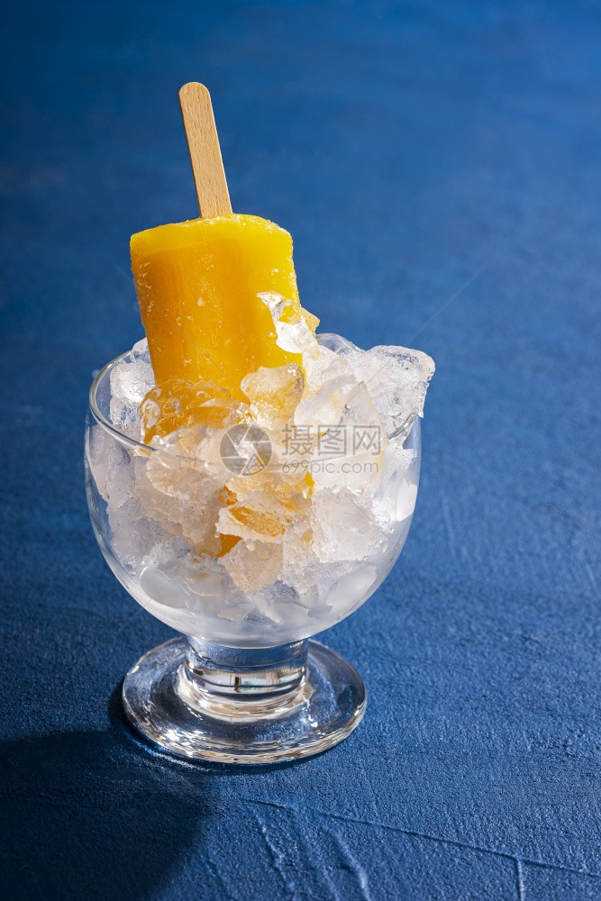 在一杯子里冷却新鲜的橙色冰棒在经典的蓝色桌子上冷的热带甜点夏天的棒子上橙色冰淇淋图片