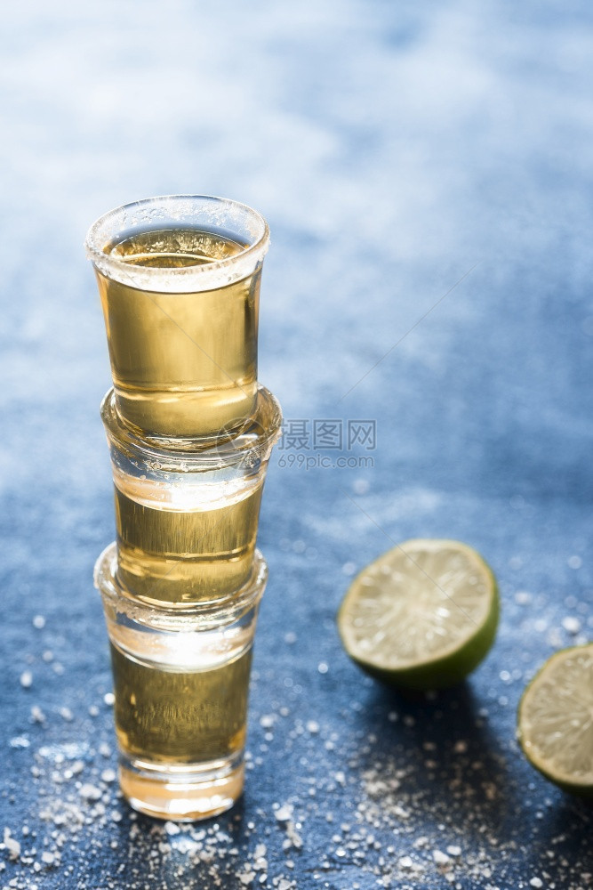 三杯龙舌兰酒堆在蓝桌上金龙舌兰酒杯加石灰和盐香味强烈的墨西哥酒精派对的镜头图片