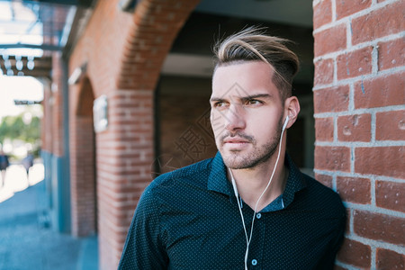英俊的年轻男子在街上用耳机听音乐的肖像城市概念高清图片