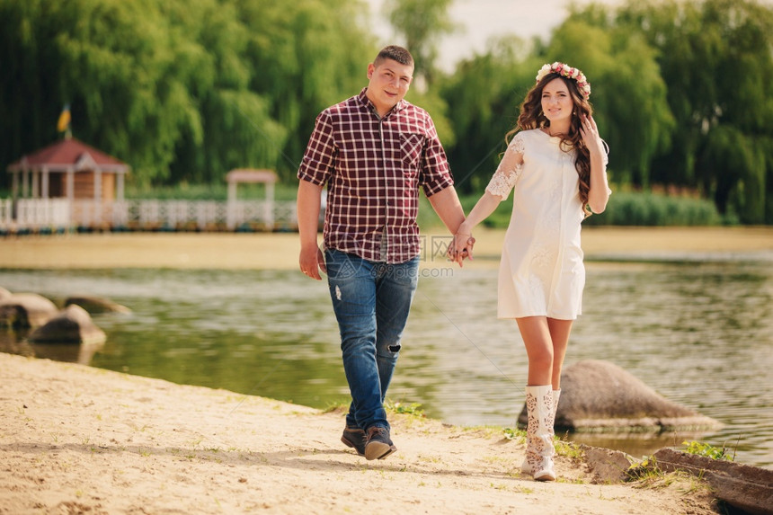 快乐的怀孕夫妇在夏季公园湖边行走图片