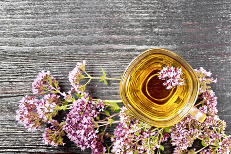 玻璃杯中的树胶草药茶上面木板背景的鲜粉红马约兰花图片