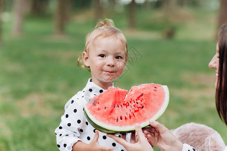 抱西瓜的小孩快乐的母亲和女儿在夏季公园吃西瓜快乐的笑脸家庭在公园吃西瓜母亲和女儿一起度过时间饮食维生素健康食品概念选择关注饮食健康品概念选择背景