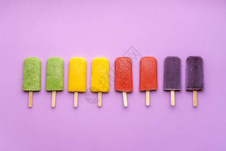 橙色冰棒紫色背景的水果冰淇淋系列平躺着彩虹冰淇淋贴在棍子上夏季新鲜甜点素食软糖背景