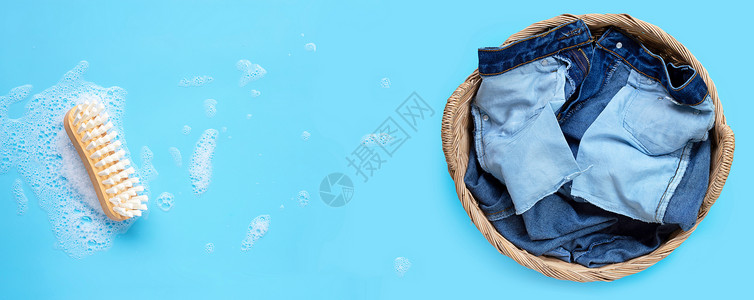 洗衣篮中的牛仔裤和洗涤衣物的木梳子放在蓝色背景的粉末洗涤水溶解泡沫上图片