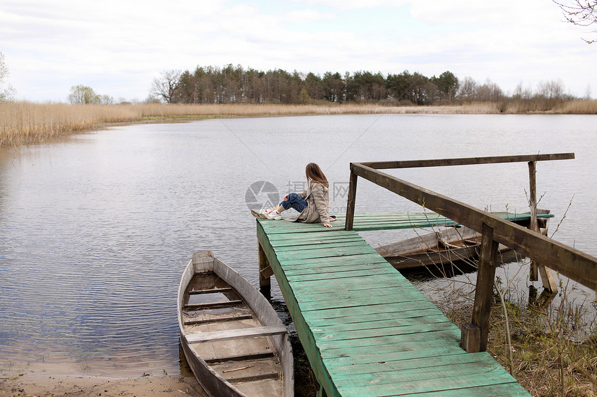 年轻美女在春天坐河边的木桥上海岸附近的老船有选择聚焦点有选择聚焦点图片
