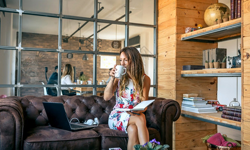 女商人喝咖啡坐在办公室的沙发上工作女商人喝咖啡在同事办公室工作图片