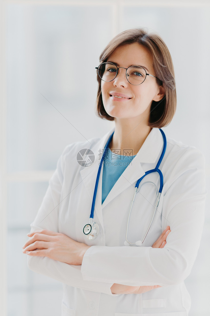 有自信的黑发女医生或外科站着双手交叉穿白制服关心随时愿意提供咨询的病人健康职业概念图片