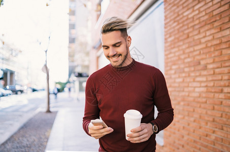 年轻英俊男子使用手机在街上举着咖啡杯户外的高清图片素材