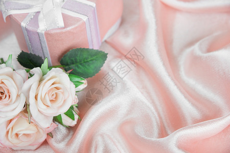 粉红玫瑰花束和礼品盒在卷粉丝织物背景上弓首带副本空格的贺卡白图片