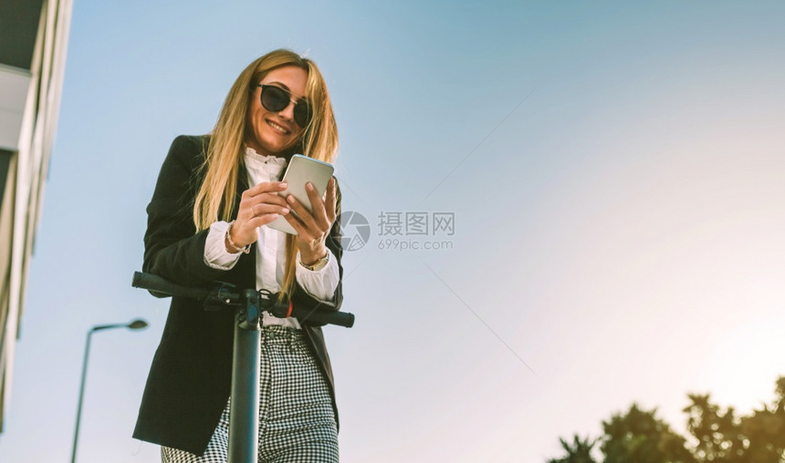 女商人靠着她的电动摩托车看着街上的手机图片
