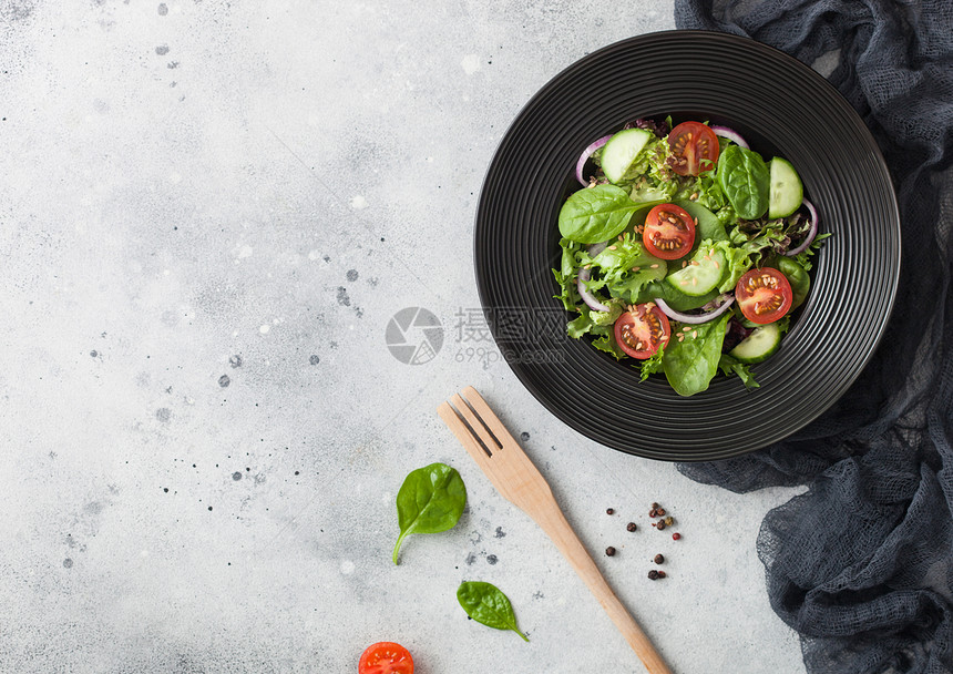 新鲜的健康素蔬菜沙拉配有生和西红柿洋葱以及黑碗的菠菜桌底面有叉和厨房布图片