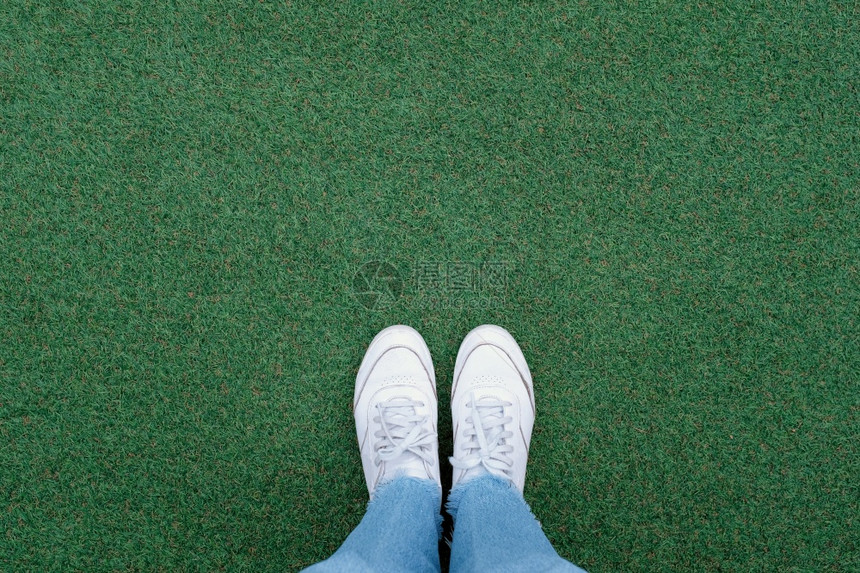 穿白色运动鞋的自足穿着绿色草地背景有复制空间春季和夏有时尚生活方式概念图片