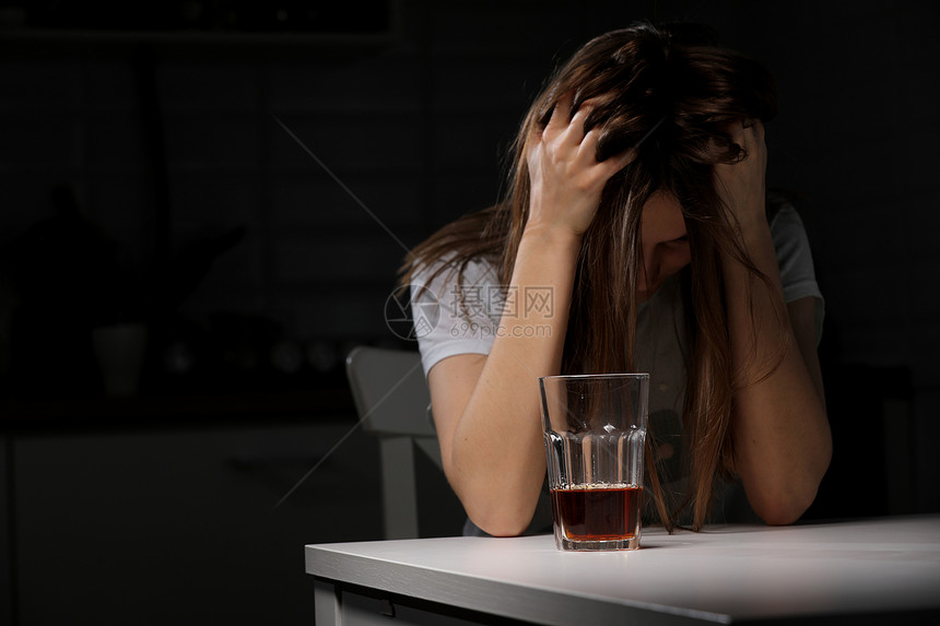 妇女在厨房饮酒患有严重头痛或偏和的年轻妇女与威士忌坐在厨房酒精依赖患有严重头痛或偏的年轻妇女与威士忌坐在厨房酗酒依赖图片