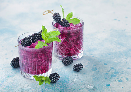 夏季装上市清凉的夏季鸡尾酒黑莓装在晶玻璃杯中冰块和薄荷装在蓝色背景上苏打汽水和酒精混合背景