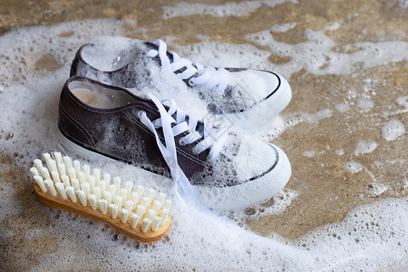 装有粉末洗涤水溶解泡沫的运动鞋和水泥地板上的木刷子洗脏鞋背景图片