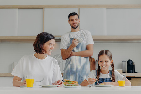 父亲站在后面为家庭准备美味的菜盘友善家庭成员周末在厨房聚会享受愉快的谈话背景图片