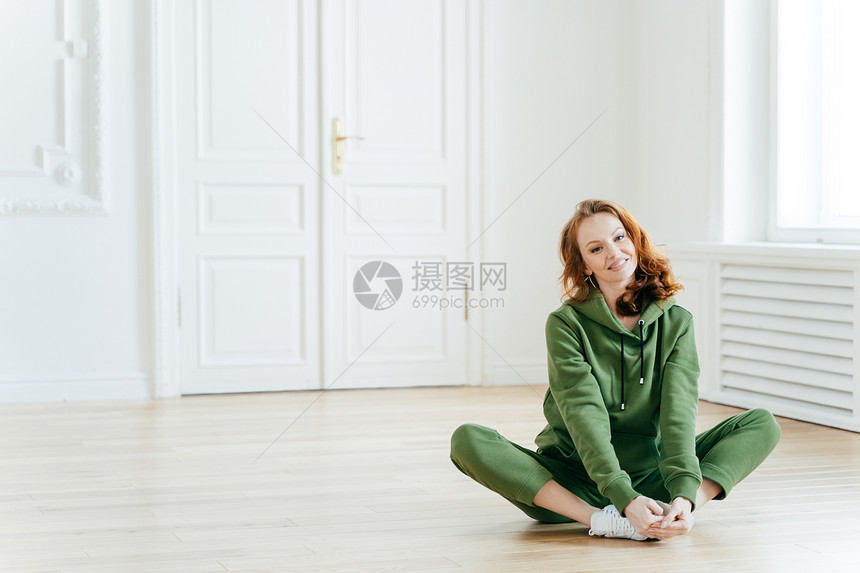 红发女喜悦的照片坐在莲花的姿势上穿运动服身体材好头发卷地板上摆姿势复制宣传内容的空间图片